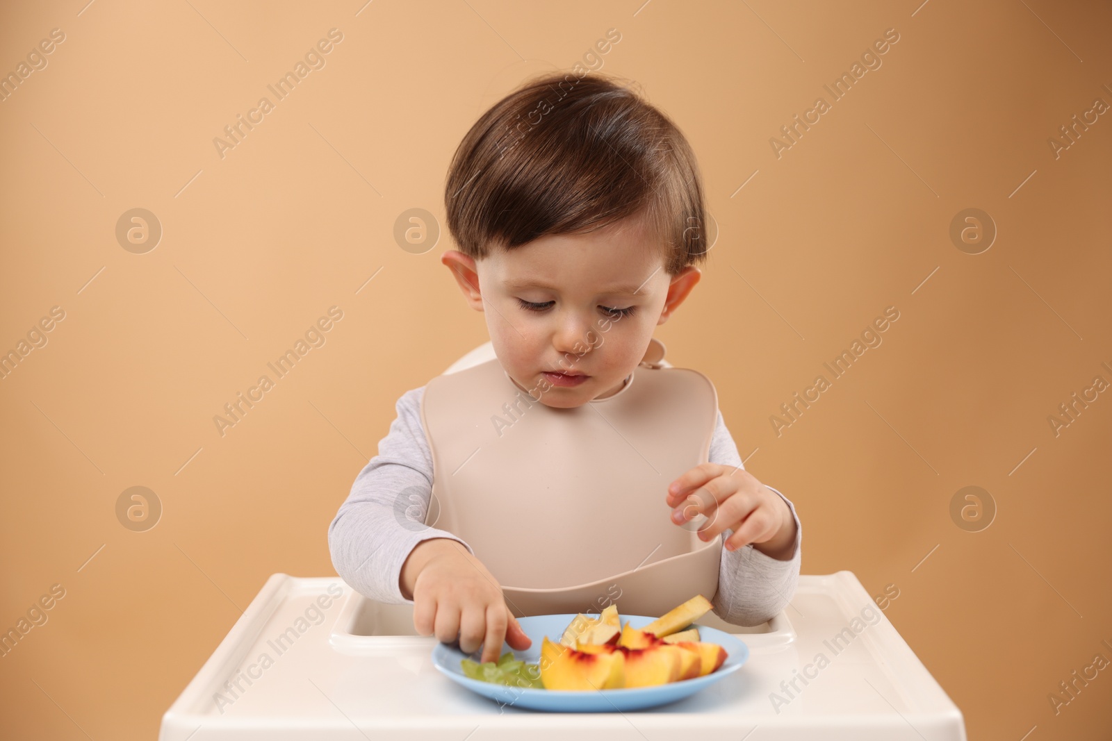 Photo of Healthy baby food. Cute little kid eating fruits in high chair on beige background