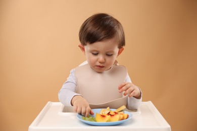 Photo of Healthy baby food. Cute little kid eating fruits in high chair on beige background