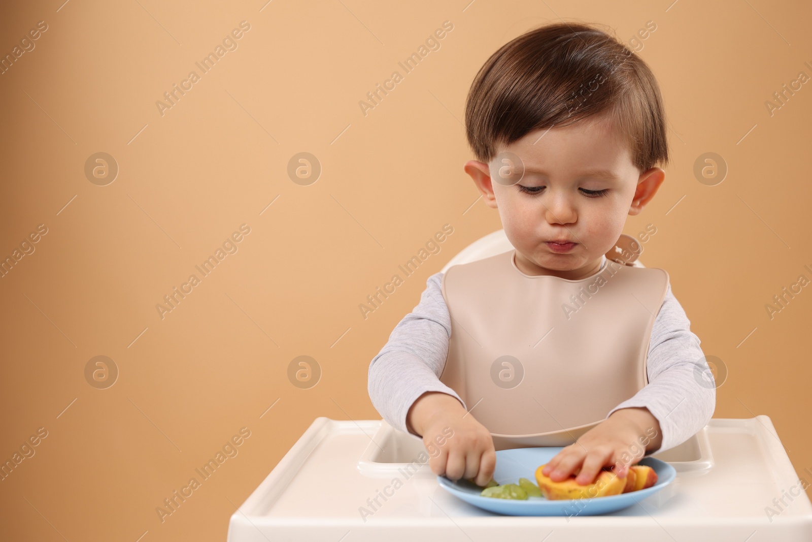 Photo of Healthy baby food. Cute little kid eating fruits in high chair on beige background, space for text