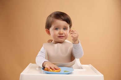 Healthy baby food. Cute little kid eating fruits in high chair on beige background