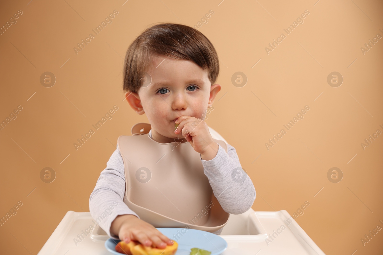 Photo of Healthy baby food. Cute little kid eating fruits in high chair on beige background