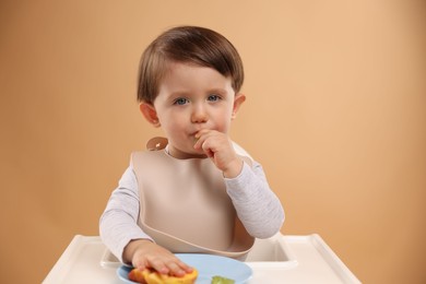 Photo of Healthy baby food. Cute little kid eating fruits in high chair on beige background