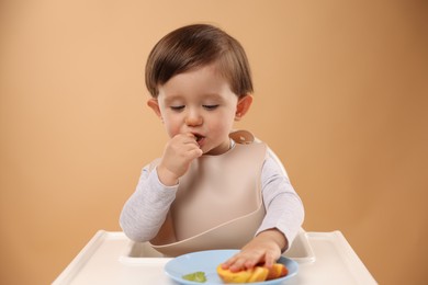 Healthy baby food. Cute little kid eating fruits in high chair on beige background