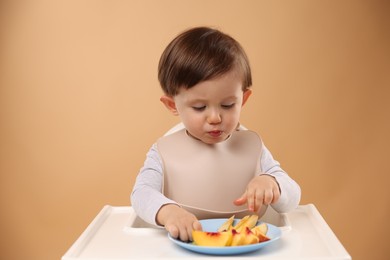 Photo of Healthy baby food. Cute little kid eating fruits in high chair on beige background