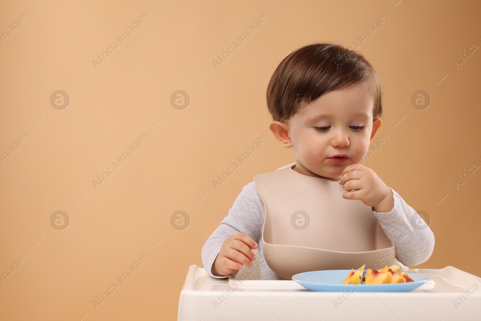 Photo of Healthy baby food. Cute little kid eating fruits in high chair on beige background, space for text