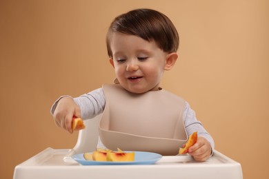 Healthy baby food. Cute little kid eating fruits in high chair on beige background