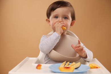 Photo of Healthy baby food. Cute little kid eating fruits in high chair on beige background