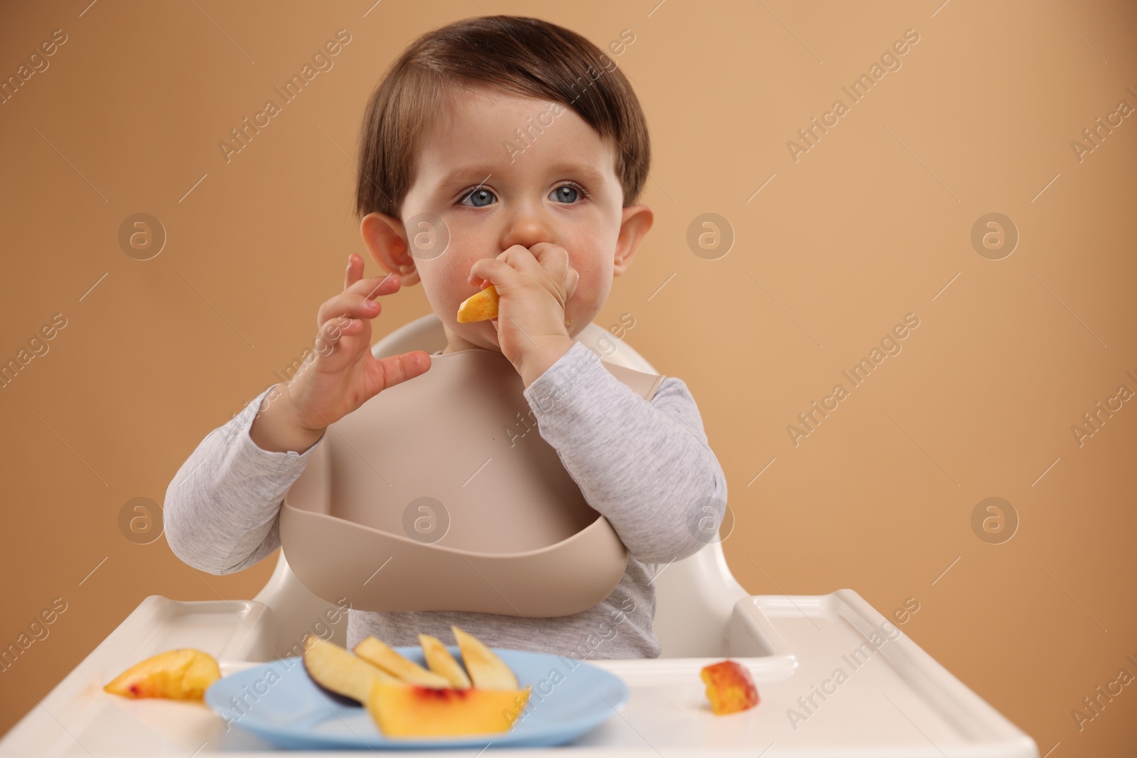 Photo of Healthy baby food. Cute little kid eating fruits in high chair on beige background