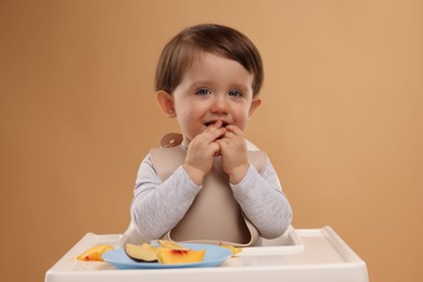 Photo of Healthy baby food. Cute little kid eating fruits in high chair on beige background