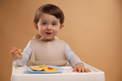 Healthy baby food. Cute little kid eating fruits in high chair on beige background