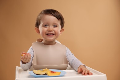 Photo of Healthy baby food. Cute little kid eating fruits in high chair on beige background