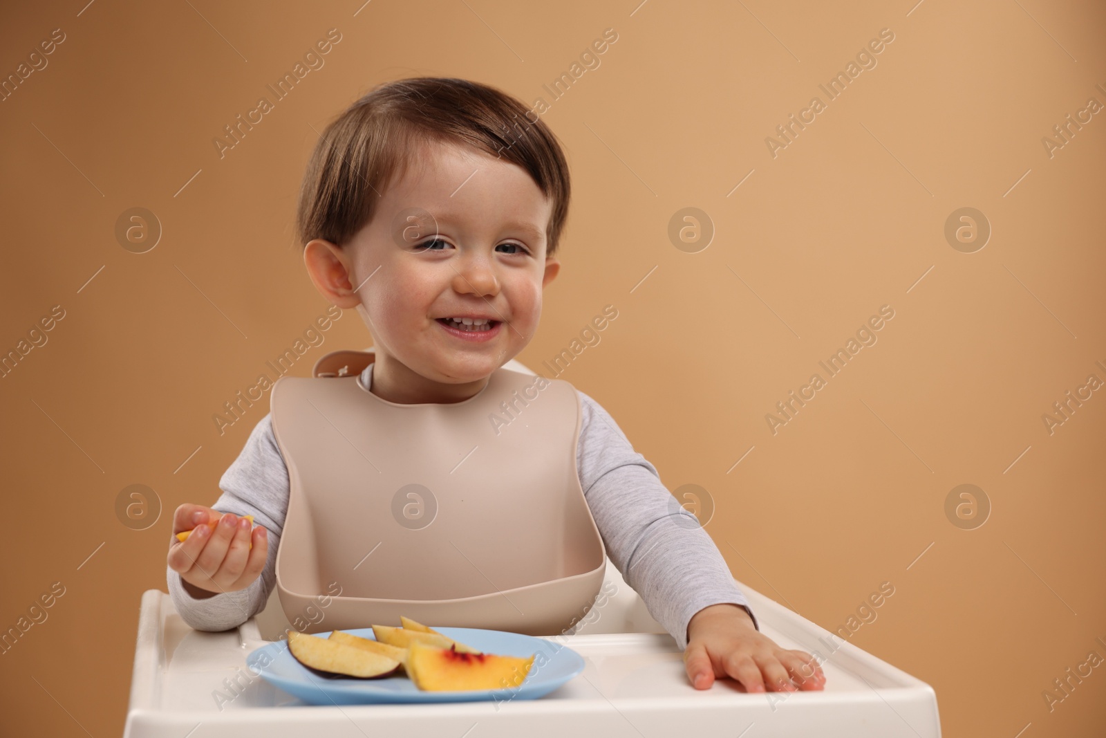 Photo of Healthy baby food. Cute little kid eating fruits in high chair on beige background