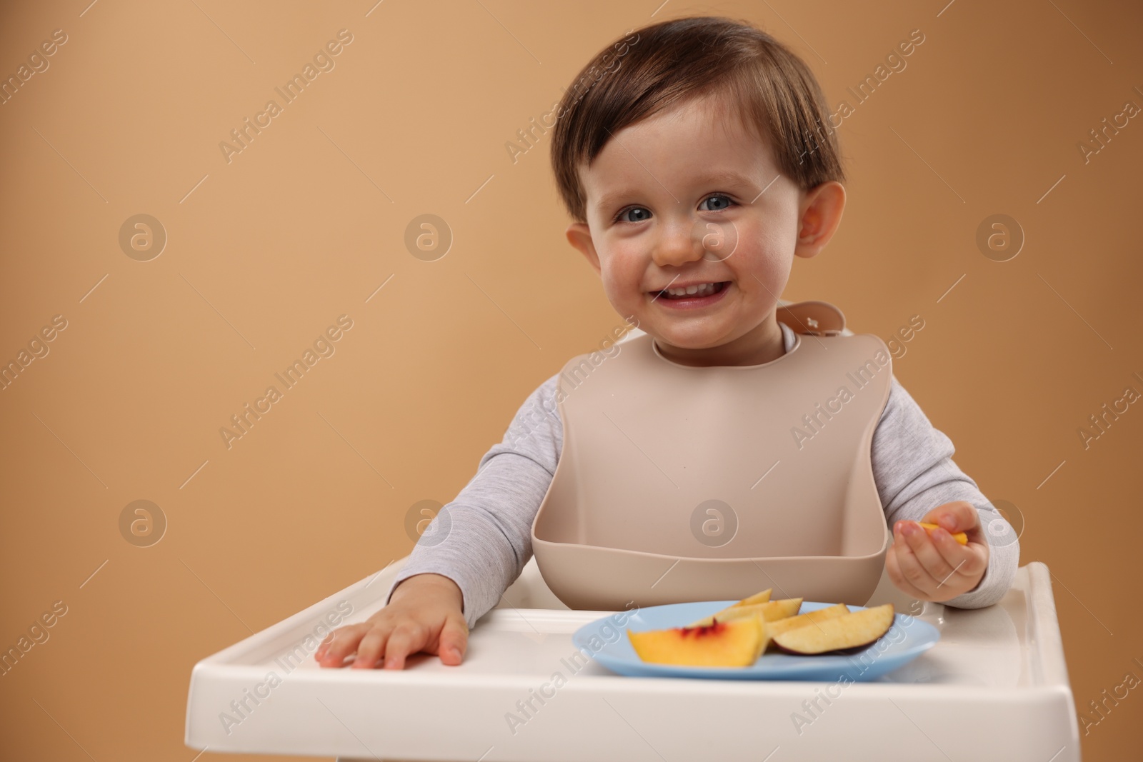 Photo of Healthy baby food. Cute little kid eating fruits in high chair on beige background, space for text