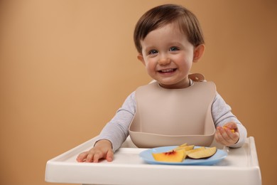 Healthy baby food. Cute little kid eating fruits in high chair on beige background, space for text