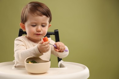 Photo of Cute little baby eating healthy food from bowl in high chair on olive background, space for text