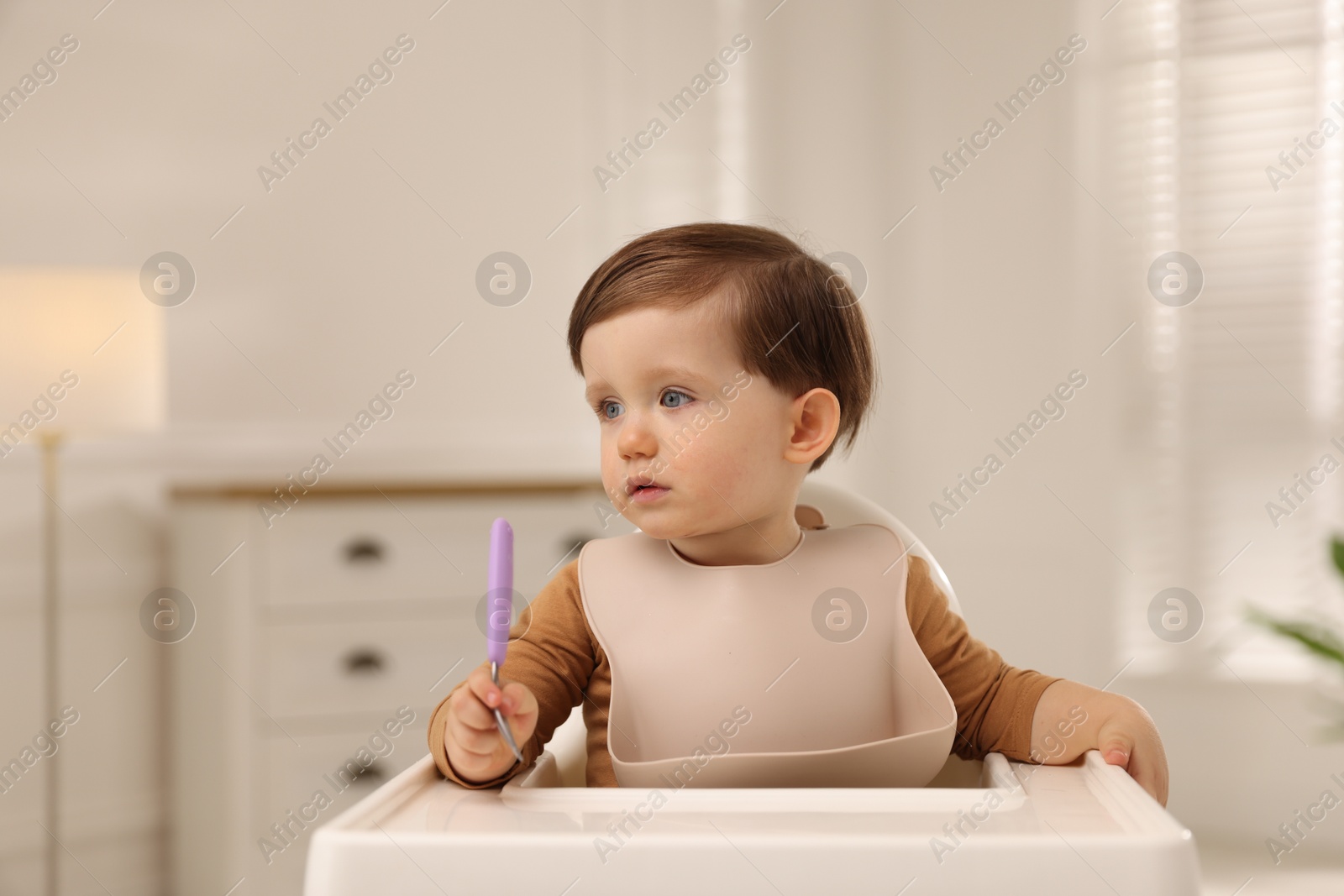 Photo of Cute little kid with fork sitting in high chair at home