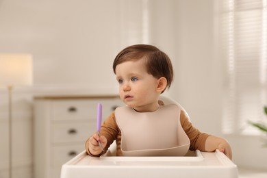 Photo of Cute little kid with fork sitting in high chair at home