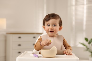 Photo of Cute little baby eating healthy food from bowl in high chair at home