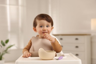 Photo of Cute little baby eating healthy food from bowl in high chair at home