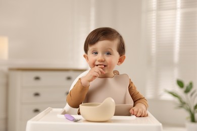 Photo of Cute little baby eating healthy food from bowl in high chair at home