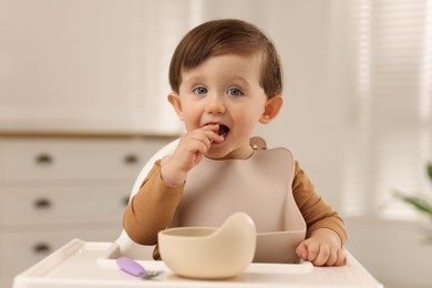 Photo of Cute little baby eating healthy food from bowl in high chair at home