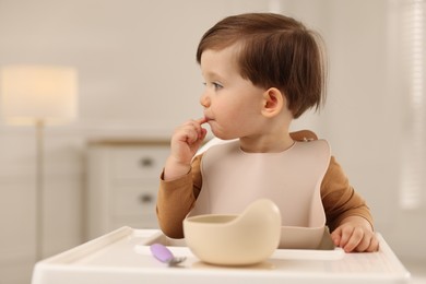 Cute little baby eating healthy food from bowl in high chair at home