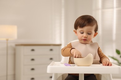 Cute little baby eating healthy food from bowl in high chair at home, space for text