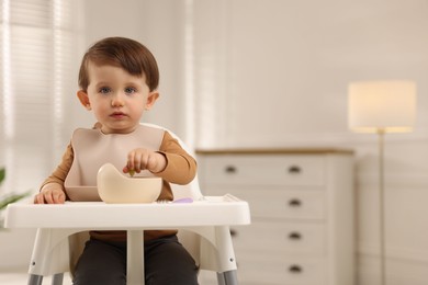 Cute little baby eating healthy food from bowl in high chair at home, space for text