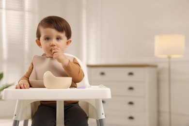 Photo of Cute little baby eating healthy food from bowl in high chair at home, space for text