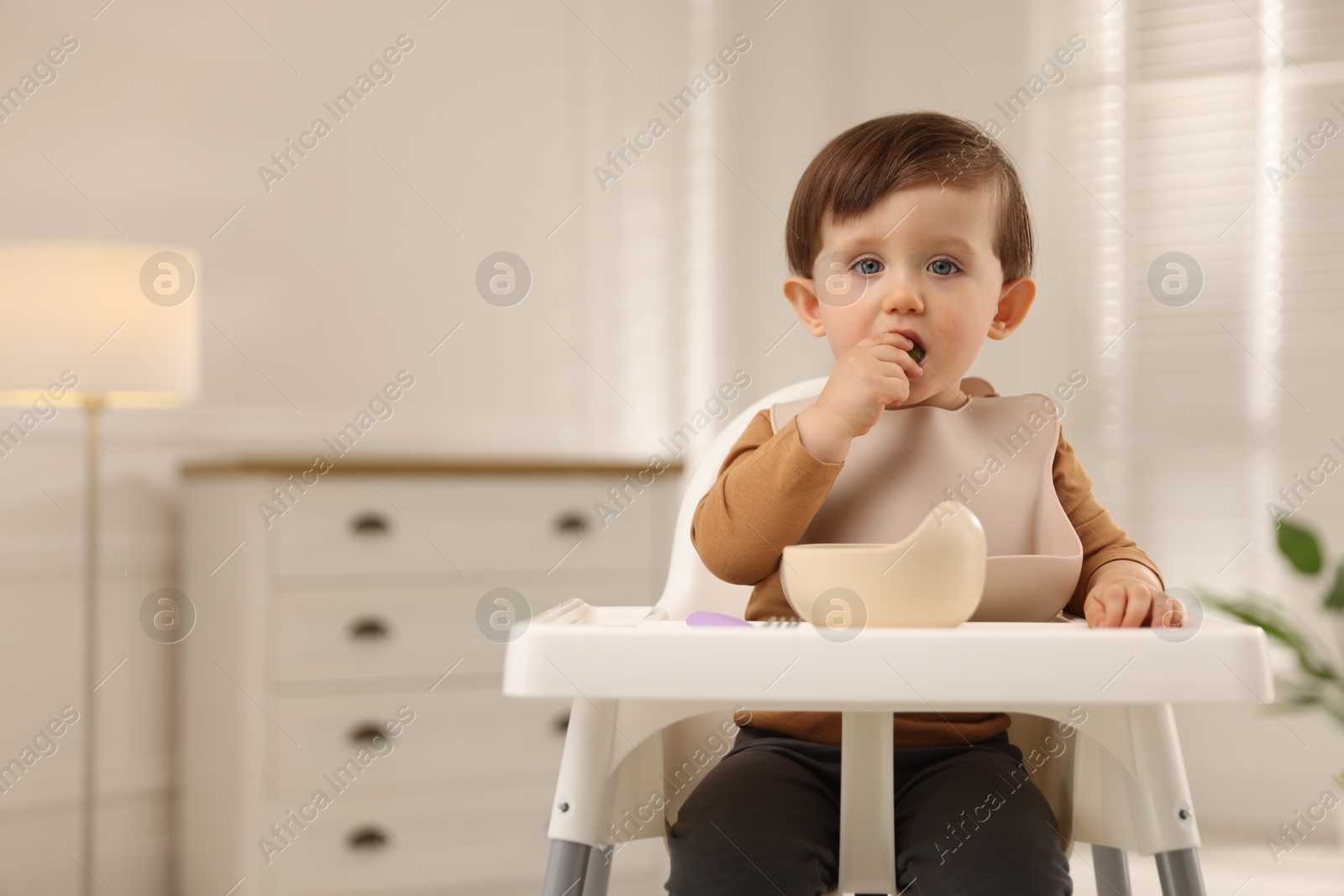 Photo of Cute little baby eating healthy food from bowl in high chair at home, space for text