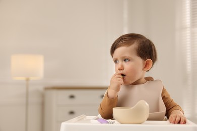 Photo of Cute little baby eating healthy food from bowl in high chair at home, space for text