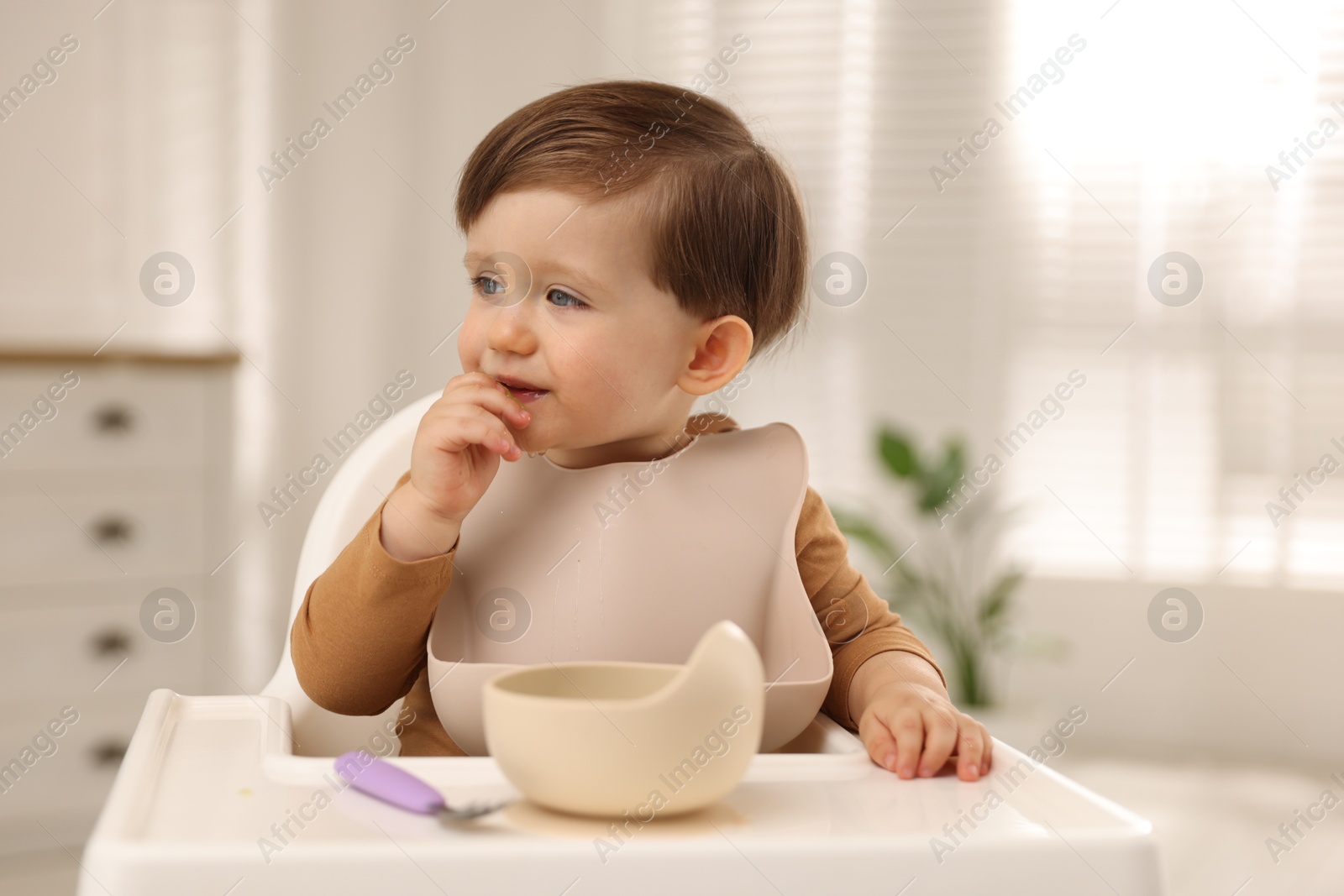 Photo of Cute little kid eating healthy baby food from bowl in high chair at home