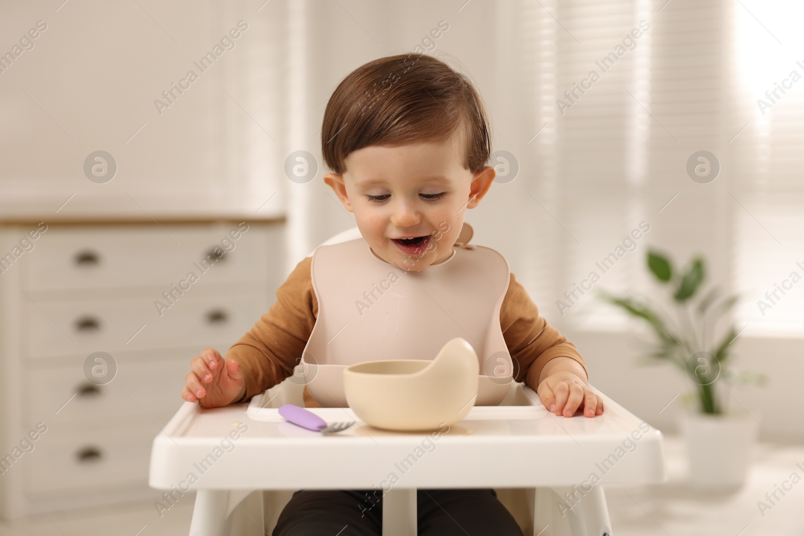 Photo of Cute little kid eating healthy baby food from bowl in high chair at home