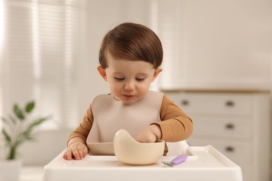 Cute little kid eating healthy baby food from bowl in high chair at home