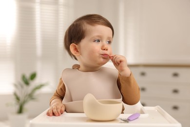 Photo of Cute little kid eating healthy baby food from bowl in high chair at home