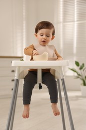 Cute little kid eating healthy baby food from bowl in high chair at home