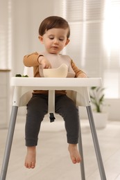 Photo of Cute little kid eating healthy baby food from bowl in high chair at home