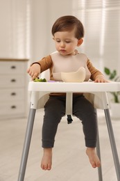 Cute little baby eating healthy food from bowl in high chair at home