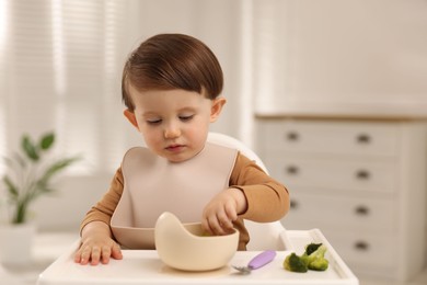 Cute little baby eating healthy food from bowl in high chair at home, space for text