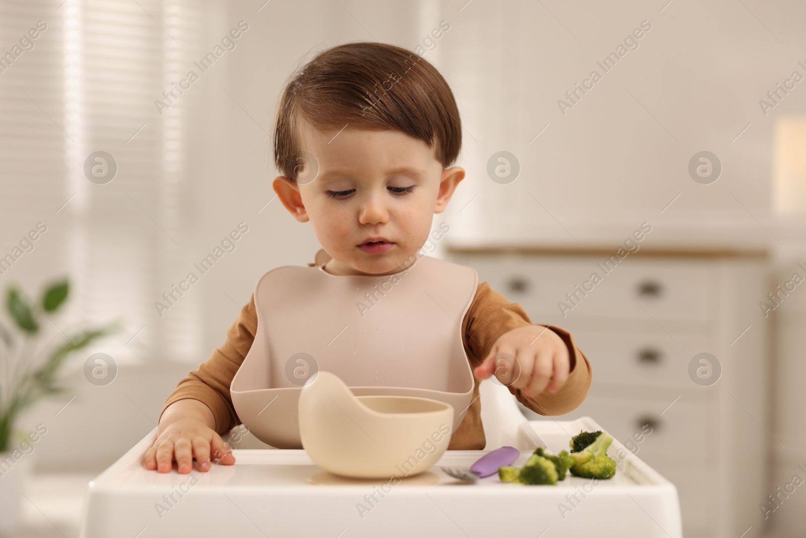 Photo of Cute little baby eating healthy food from bowl in high chair at home