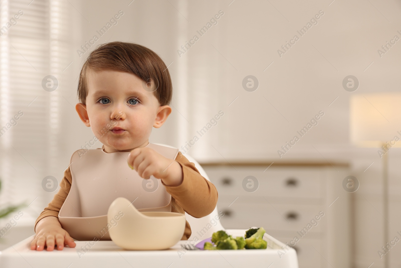 Photo of Cute little baby eating healthy food from bowl in high chair at home, space for text