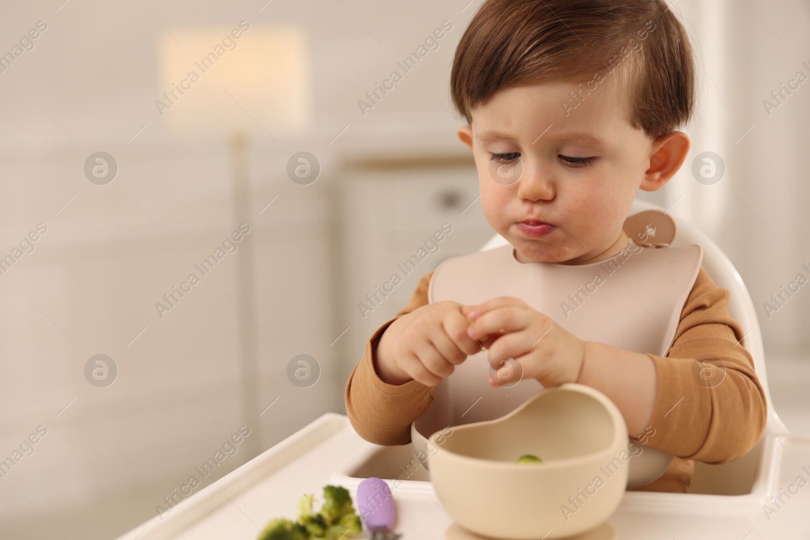 Photo of Cute little baby eating healthy food from bowl in high chair at home, space for text