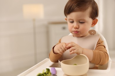 Cute little baby eating healthy food from bowl in high chair at home, space for text