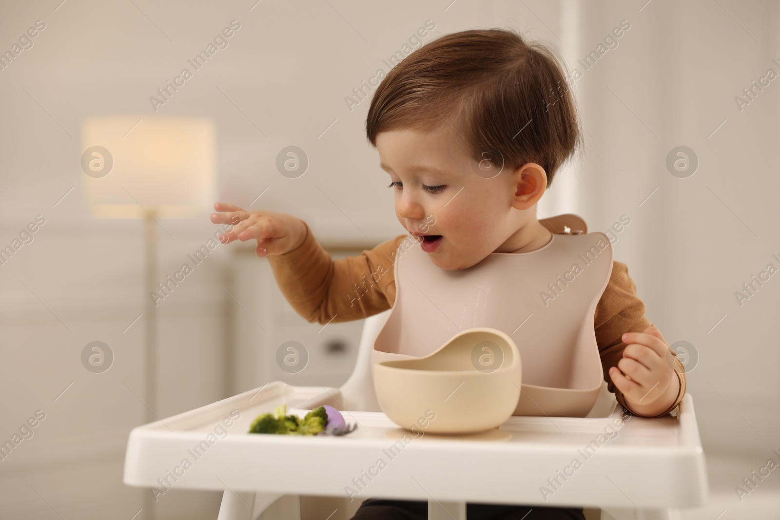 Photo of Cute little baby eating healthy food from bowl in high chair at home