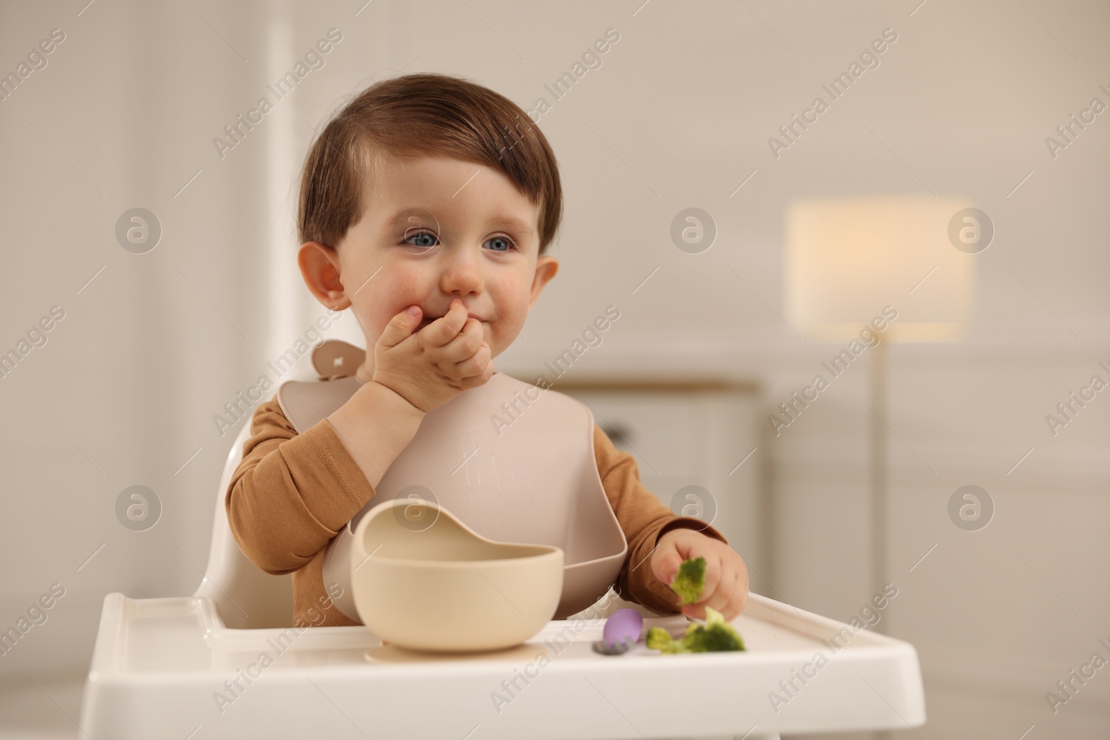 Photo of Cute little baby eating healthy food from bowl in high chair at home, space for text