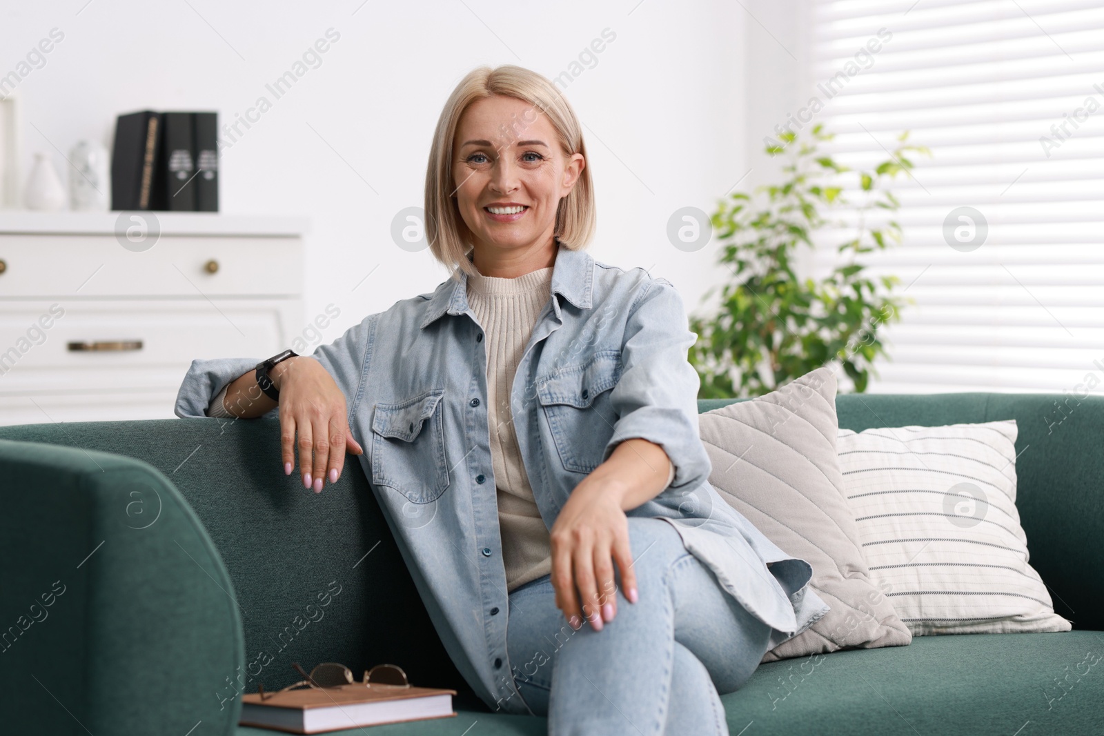 Photo of Portrait of smiling middle aged woman with book on sofa at home