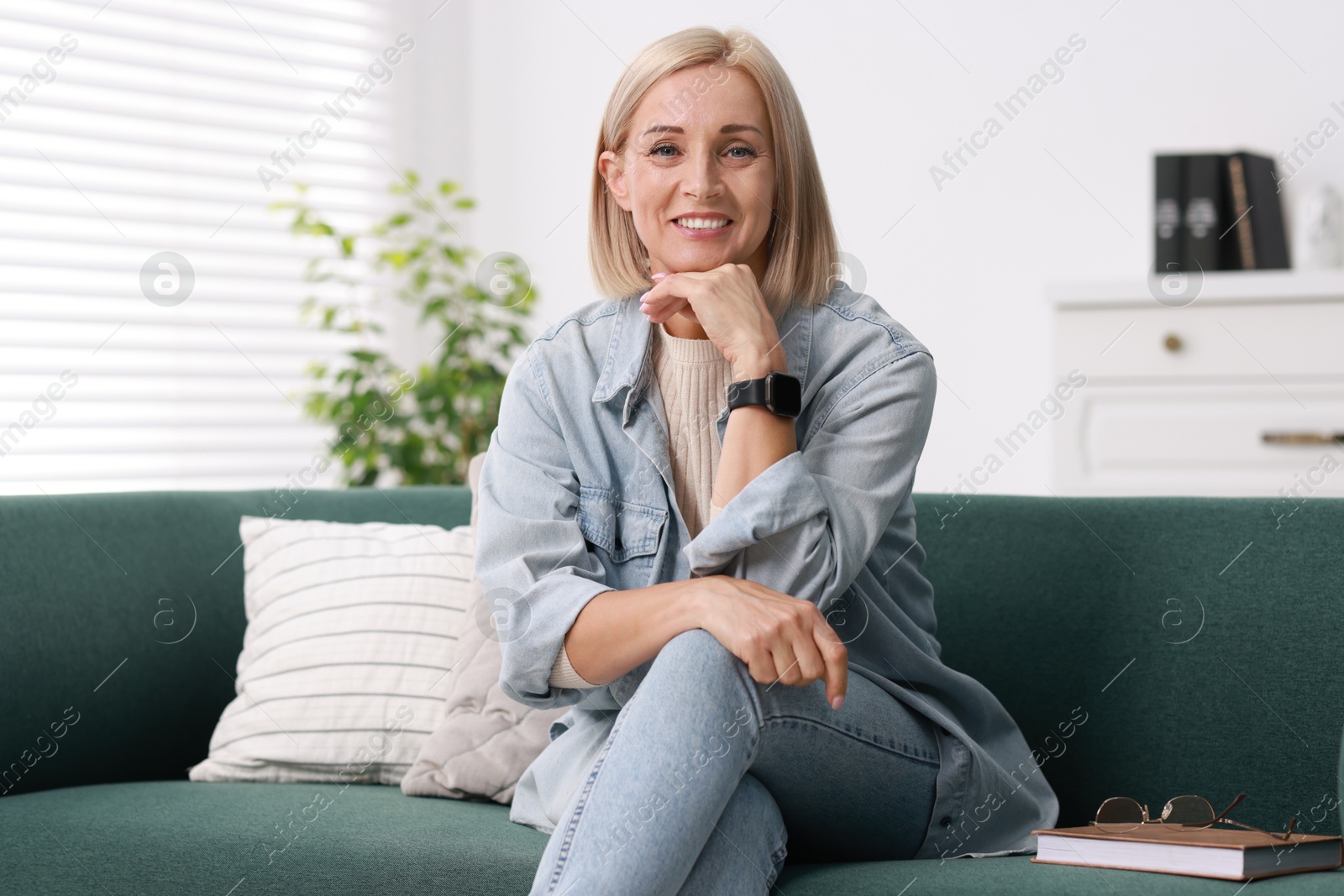 Photo of Portrait of smiling middle aged woman with book on sofa at home