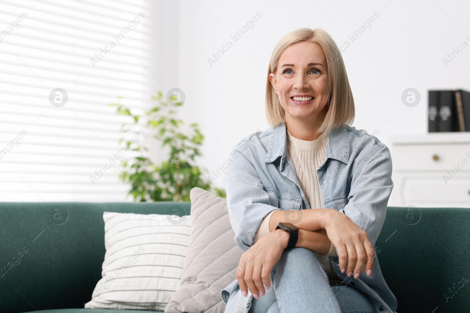 Photo of Portrait of smiling middle aged woman on sofa at home. Space for text