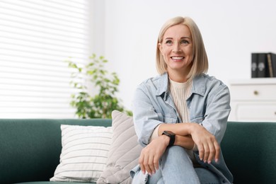 Photo of Portrait of smiling middle aged woman on sofa at home. Space for text