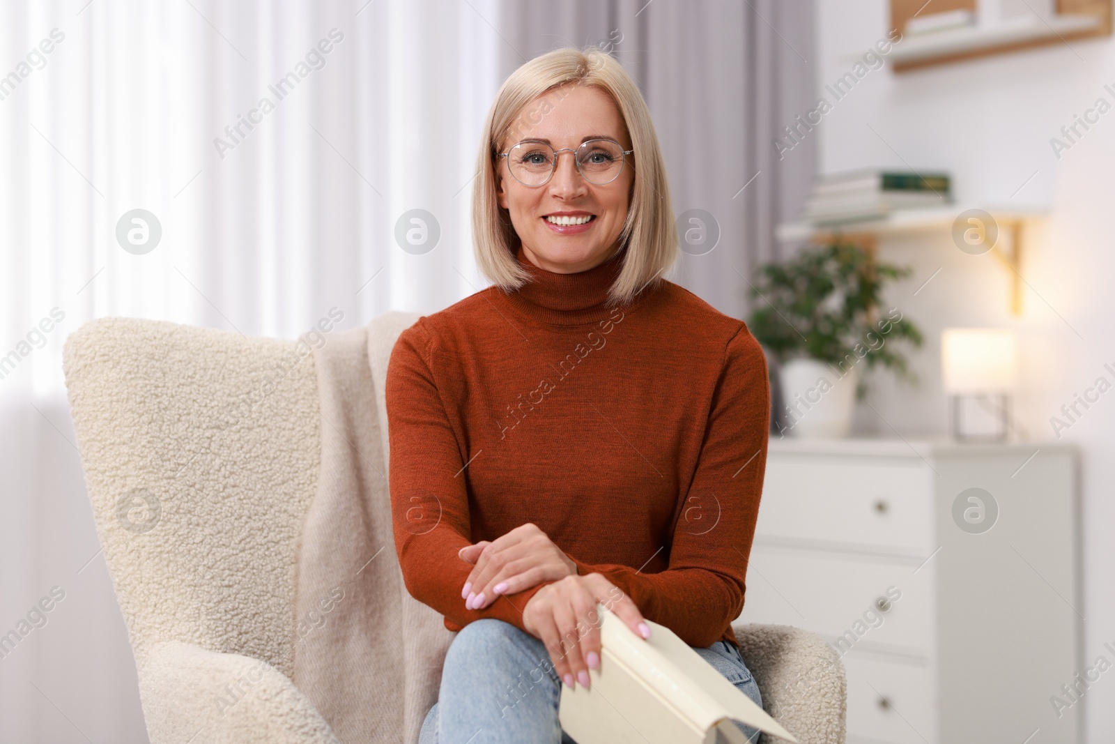 Photo of Portrait of smiling middle aged woman with book on armchair at home